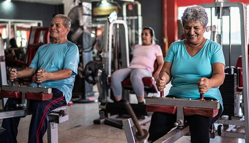 Fotografía adultos mayores haciendo ejercicio en un gimnasio utilizando máquinas de ejercicio.