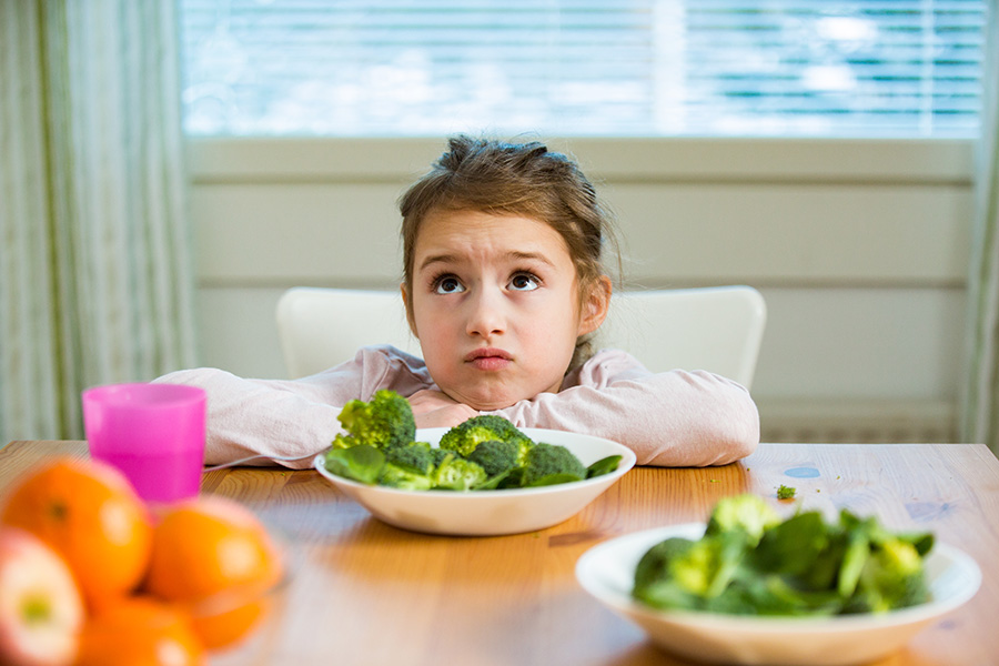 Una niña infeliz se enfrenta a un plato de brócoli.