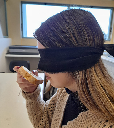 Una mujer con los ojos vendados huele un trozo de pan.