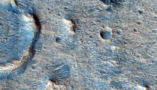 Imagen teñida de azul de una porción de la superficie de Marte, con cráteres visibles y pocks de diferentes tamaños.