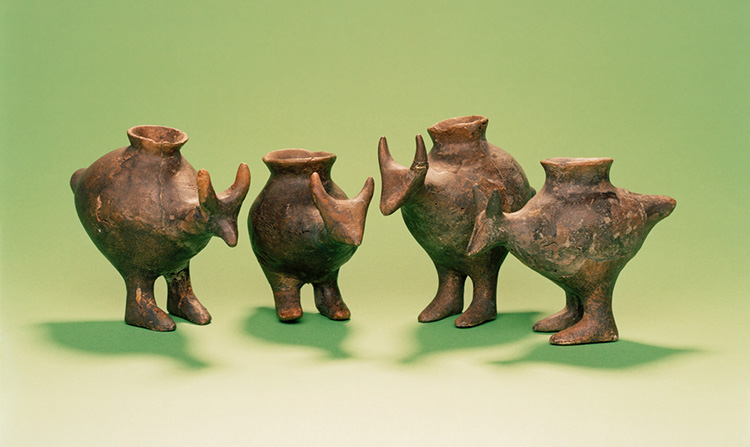 La foto muestra cuatro vasijas de cerámica, cada una con una abertura en la parte superior y con forma de animal con cabeza, orejas, dos patas y cola.