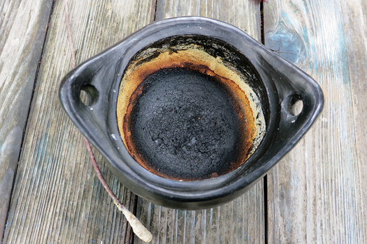 La foto muestra una vasija redonda con una capa de comida quemada y ennegrecida en el fondo.