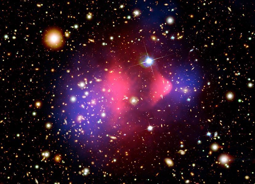 La imagen compuesta muestra el cúmulo de galaxias 1E 0657-556 a través de múltiples longitudes de onda. El gas caliente, mostrado en rosa, ha sido detectado con el telescopio de rayos X Chandra. Magellan y Hubble proporcionaron las imágenes ópticas de las galaxias en colisión. La mayor parte de la materia de la colisión es materia oscura, mostrada en azul y calculada mediante el análisis del efecto de las lentes gravitacionales.