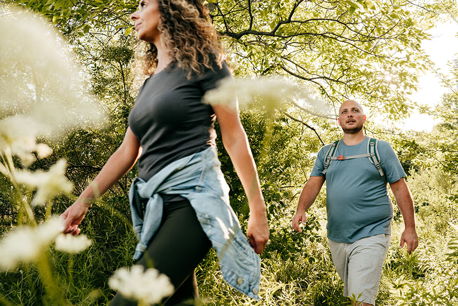 Una mujer atlética y un hombre con sobrepeso caminan por el bosque.