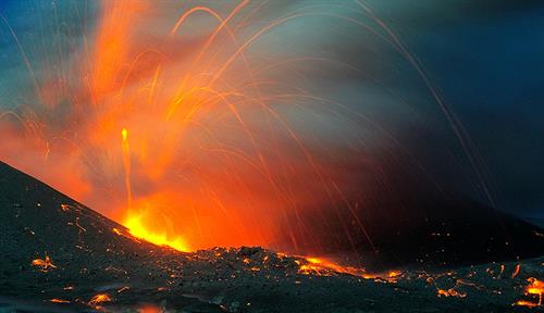 La foto muestra la lava naranja que sale de la cima de un cráter volcánico.