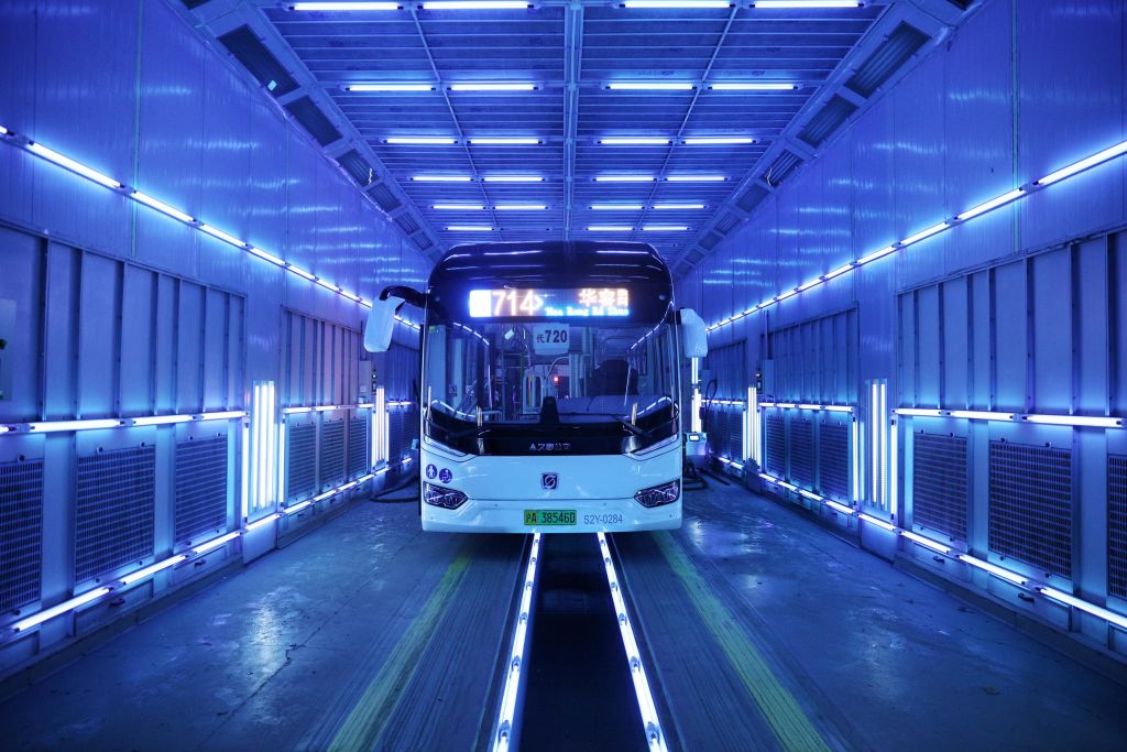 Fotografía de un autobús vacío en un túnel rodeado de lámparas que brillan en color violeta.