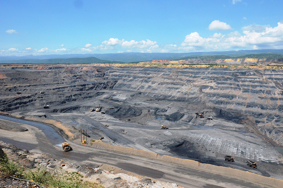 Vista panorámica de la mina de carbon a cielo abierto El Cerrejón. Bajo un cielo azul y despejado, se observan caminos circunvalares grises y varios tractores sobre esos caminos.