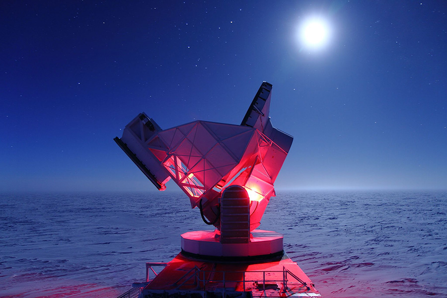 La foto muestra parte del telescopio iluminado en rojo en una noche de luna, con nieve visible hasta el horizonte.