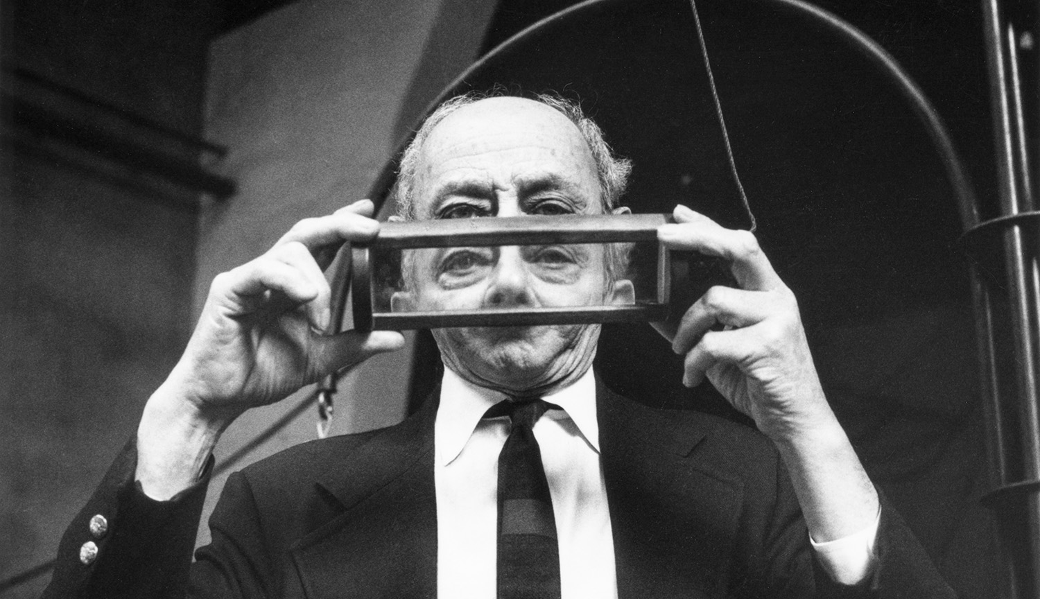 Foto de un hombre mayor sosteniendo un prisma transparente enmarcado, que bloquea y distorsiona parcialmente su rostro.