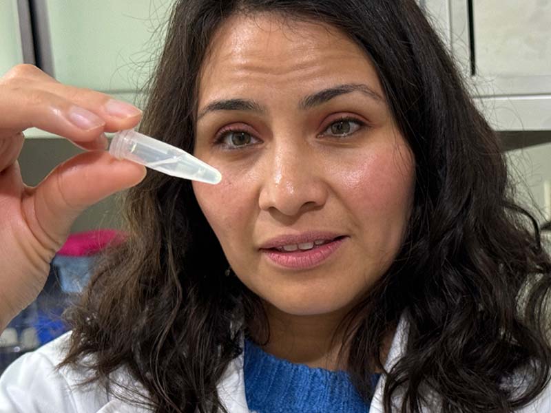 Una mujer de pelo negro y vestida con gabacha de laboratorio, sostiene una pipeta.