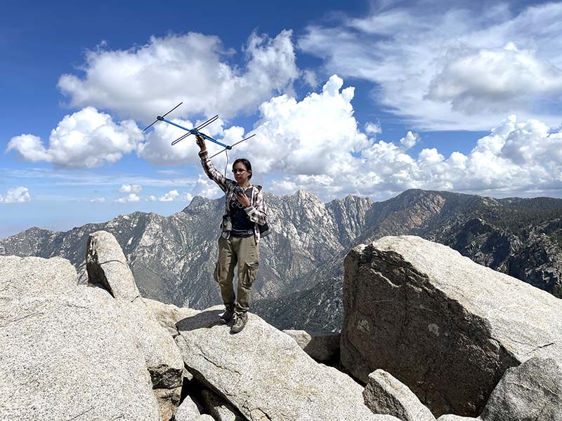 Una mujer de pie, en la cúspide de una montaña, sostiene una antena.