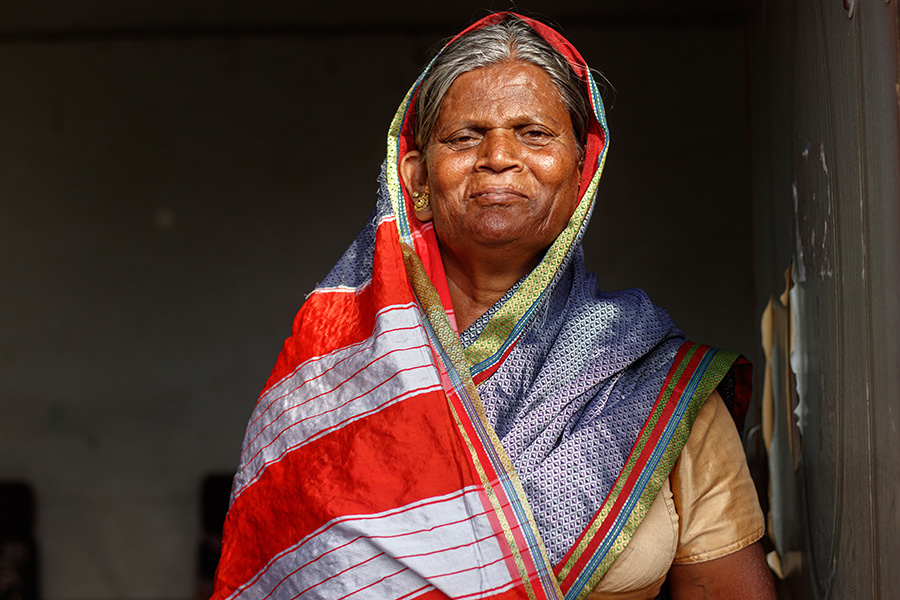 Alka Kamble Mujer con la cabeza cubierta con un pañuelo de colores, operada de cataratas tras años de trabajar bajo el sol y el calor extremos, sobre un fondo oscuro.