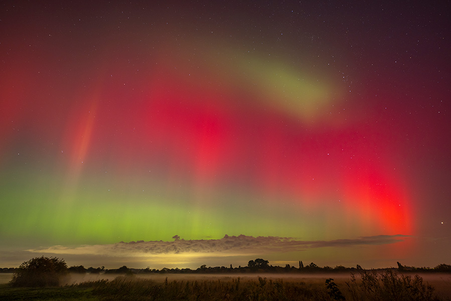 La foto muestra una cortina roja de color en el cielo del atardecer sobre un campo.