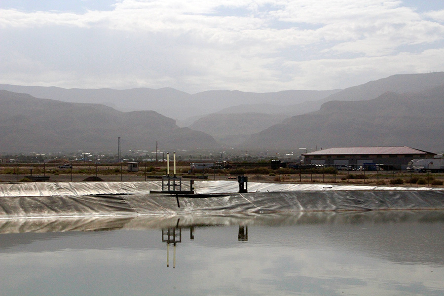 Un gran embalse de agua de aspecto sucio está respaldado por paredes blancas inclinadas. Hay montañas a lo lejos y nubes en el cielo.