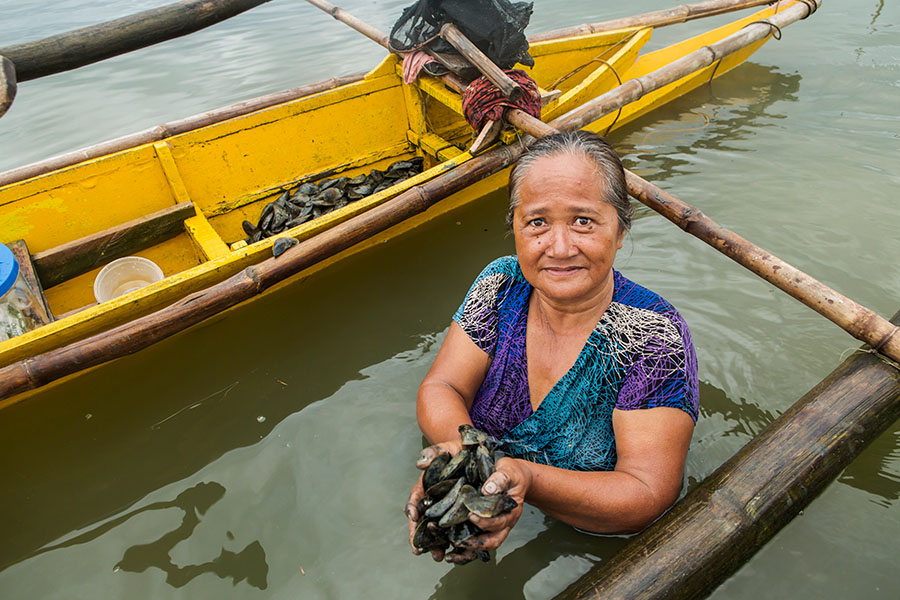 Mejillones Una mujer de pie dentro del agua, y al lado de una panga amarilla, sostiene mejillones en sus manos.