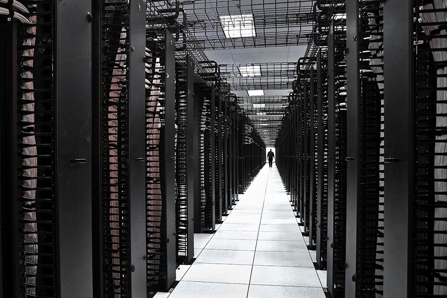 Centro de procesamiento de datos Un largo pasillo entre grandes y oscuras filas de equipos de un centro de procesamiento datos. Alguien camina por el pasillo en la distancia.