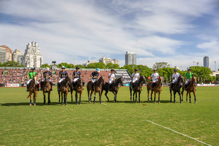 Diez caballos con sus jinetes en fila, en una cancha de polo.