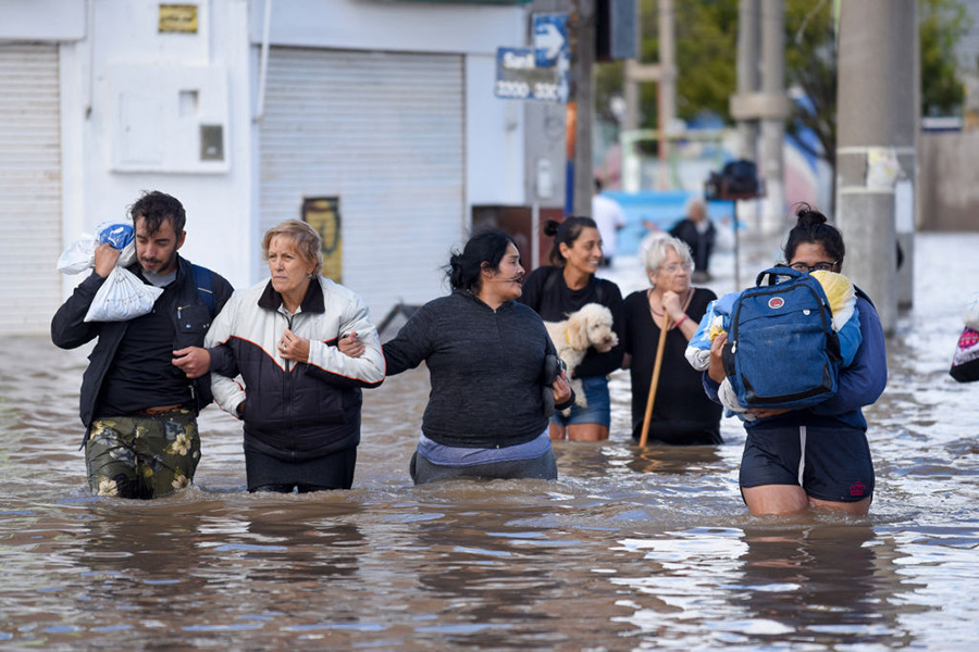 Fotografía de personas caminando por una calle inundada con agua hasta los muslos.