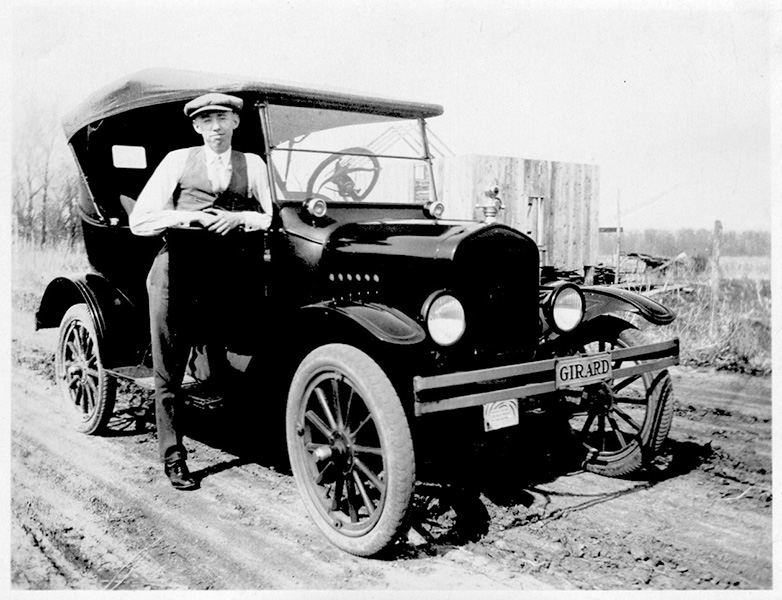 Un hombre junto a un Ford Modelo T en una foto en blanco y negro de los años veinte.