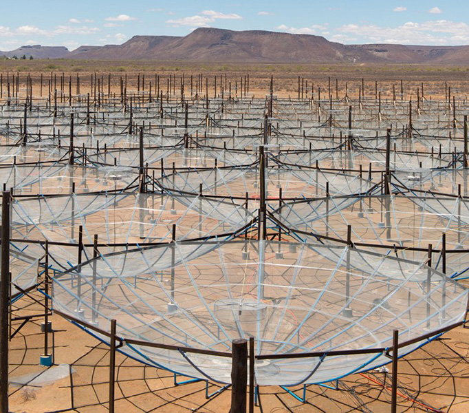 Un conjunto de telescopios que parecen paraguas transparentes, gigantes e invertidos en el desierto contra un cielo azul claro.