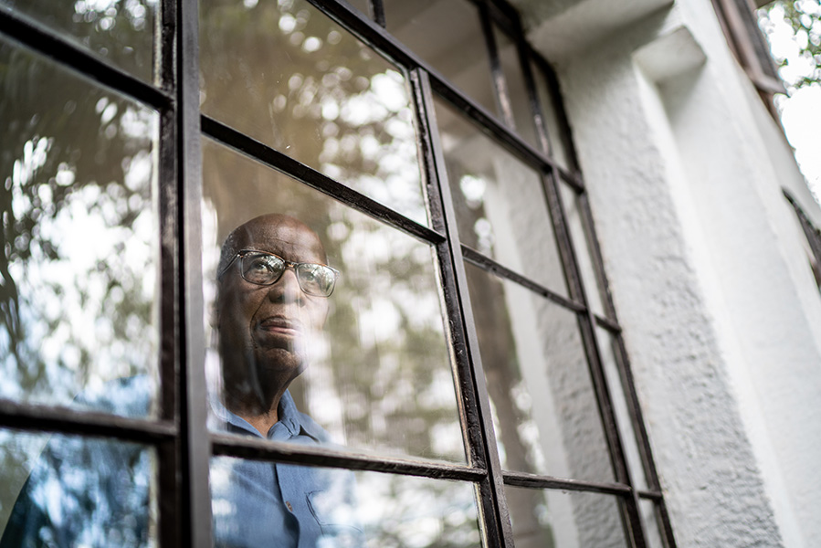 Un anciano mirando tristemente por una ventana.