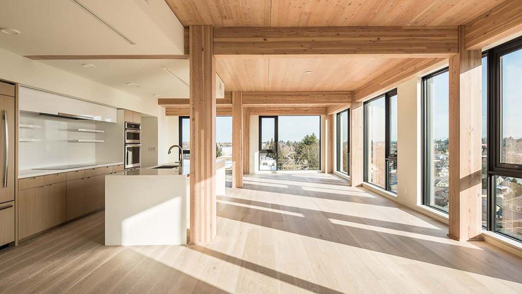 Foto del interior de un apartamento moderno con vigas, piso y techo de madera. Las ventanas dan al barrio circundante.