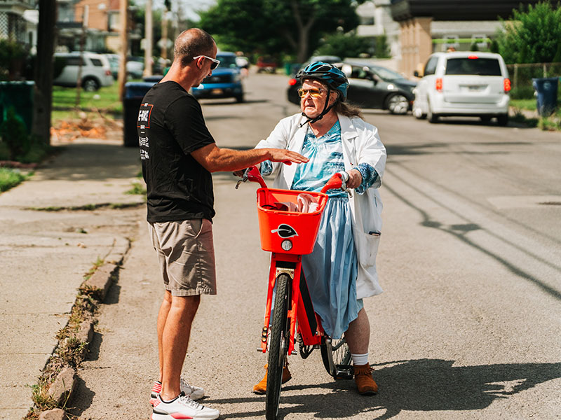 Ampliar el acceso a la movilidad compartida Una anciana en una bicicleta eléctrica habla con un hombre que está a su lado.