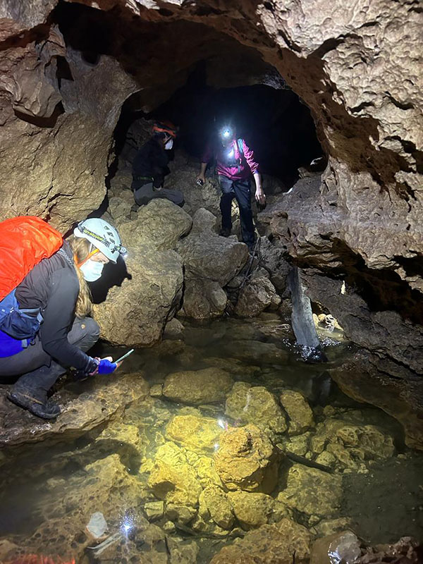 Cueva Río Subterráneo Dos personas de pie en una cueva mirando hacia el agua. Llevan luces en sus cascos.