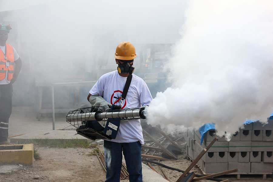 Foto de un hombre con equipo de protección fumigando una zona; salen volutas de humo del fumigador.