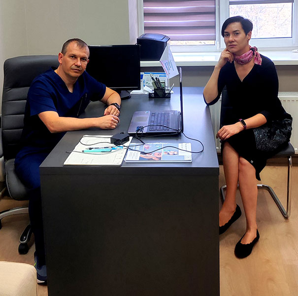 El cirujano y la microbióloga Un hombre sentado detrás de un escritorio y una mujer sentada al otro lado del escritorio, ambos con rostros sombríos.