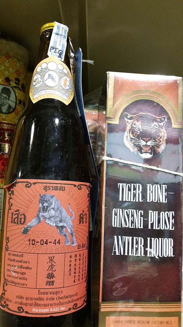 Una fotografía muestra dos productos. A la izquierda hay una botella con una etiqueta que muestra un gran felino saltando. A la derecha hay una caja con la imagen de una cara de tigre y la etiqueta “LICOR DE HUESO DE TIGRE, GINSENG Y CUERNOS DE CIERVO”.