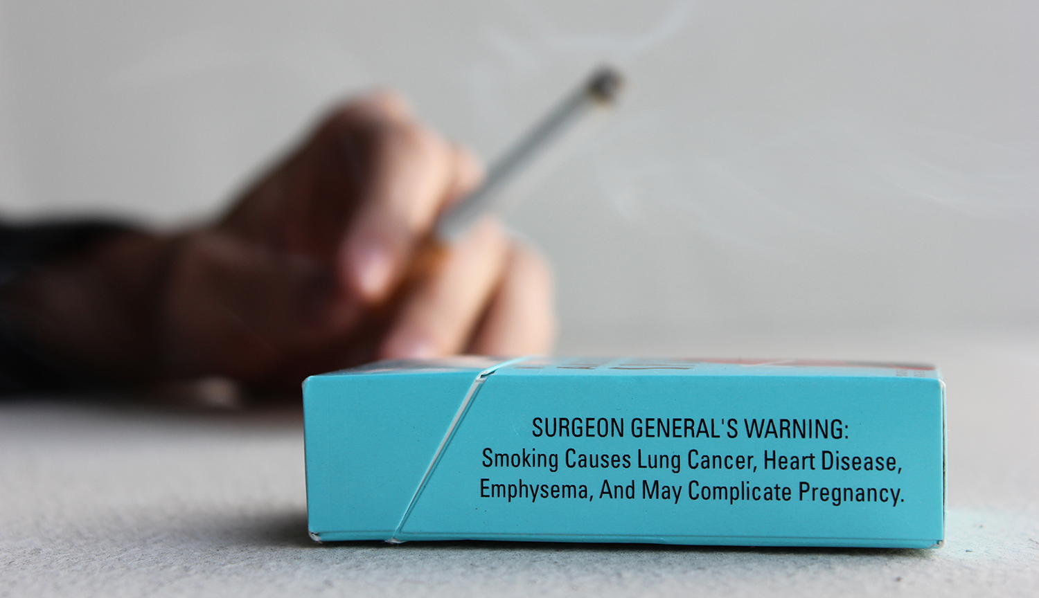 Fotografía de una etiqueta de advertencia en el lateral de un paquete de cigarrillos. Dice en inglés: ADVERTENCIA DEL CIRUJANO GENERAL: Fumar provoca cáncer de pulmón, cardiopatías, enfisema y puede complicar el embarazo.